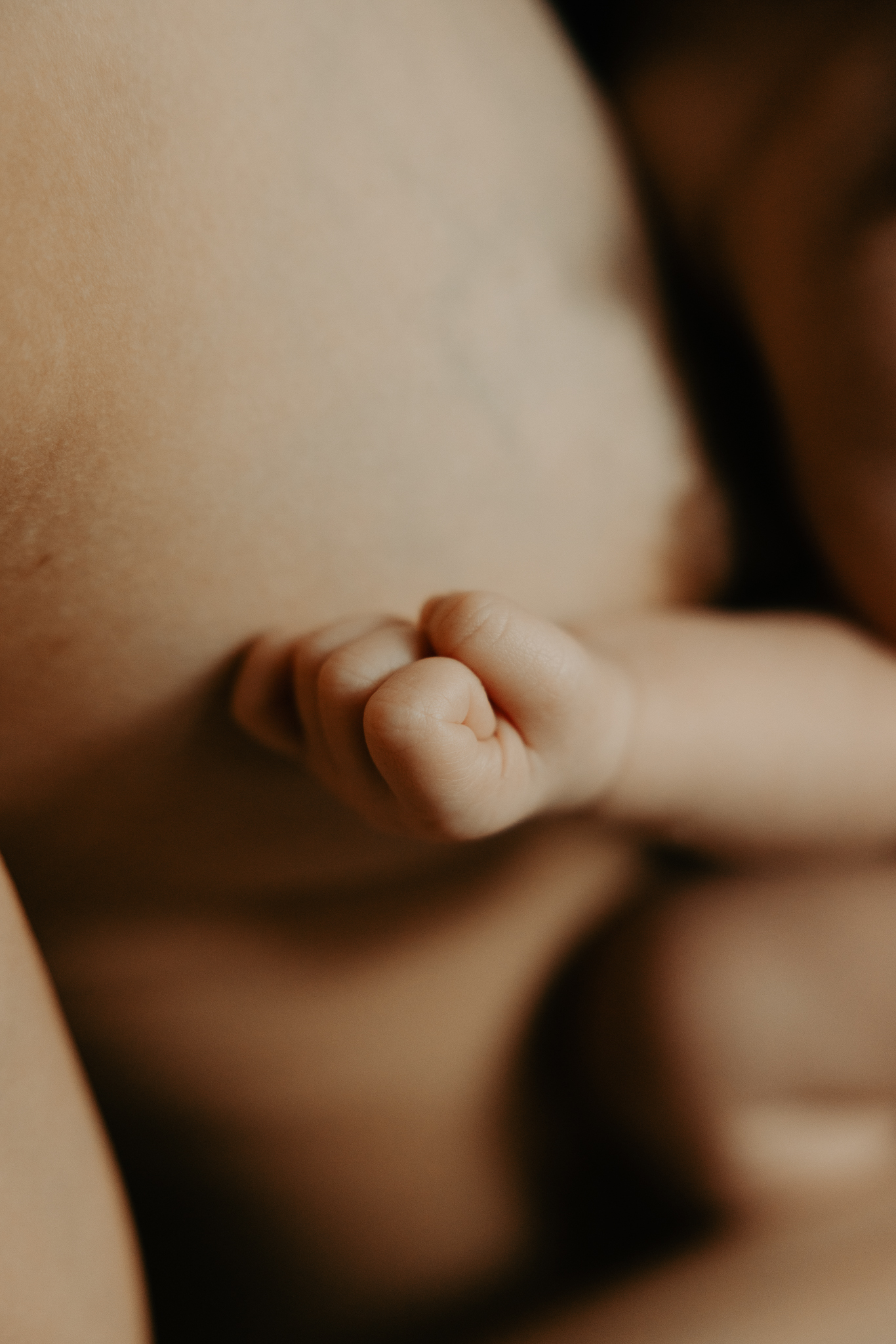 En nyfödd bebis hand ligger mot mammas bröst.