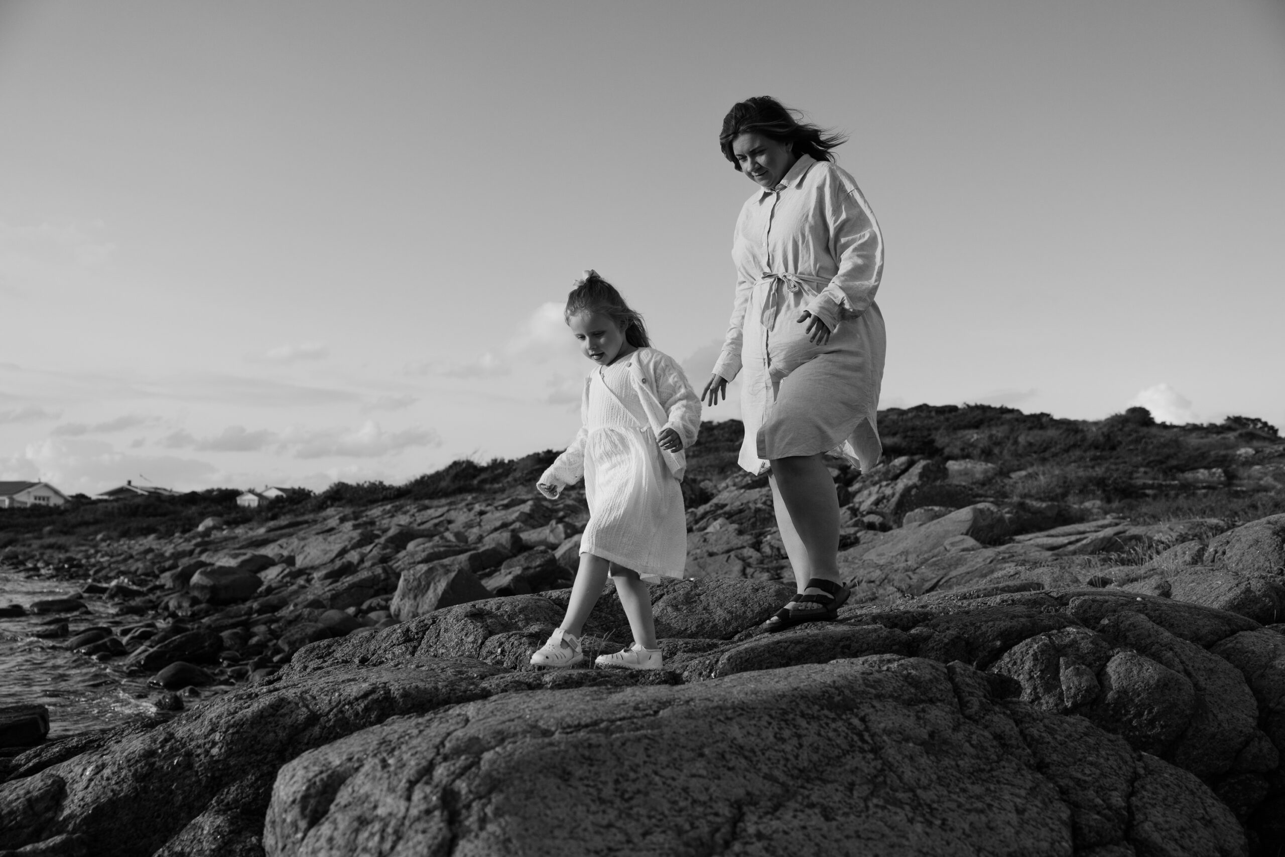 En mamma promenerar på klipporna vid havet tillsammans med sin dotter.