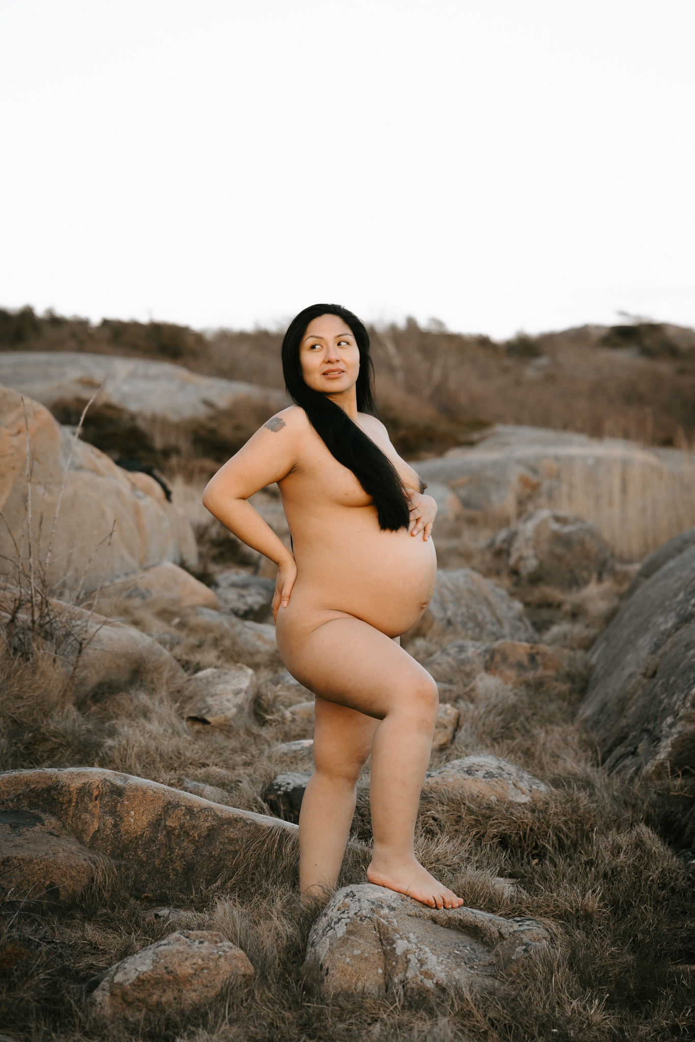 En gravid kvinna står på klipporna vid havet.