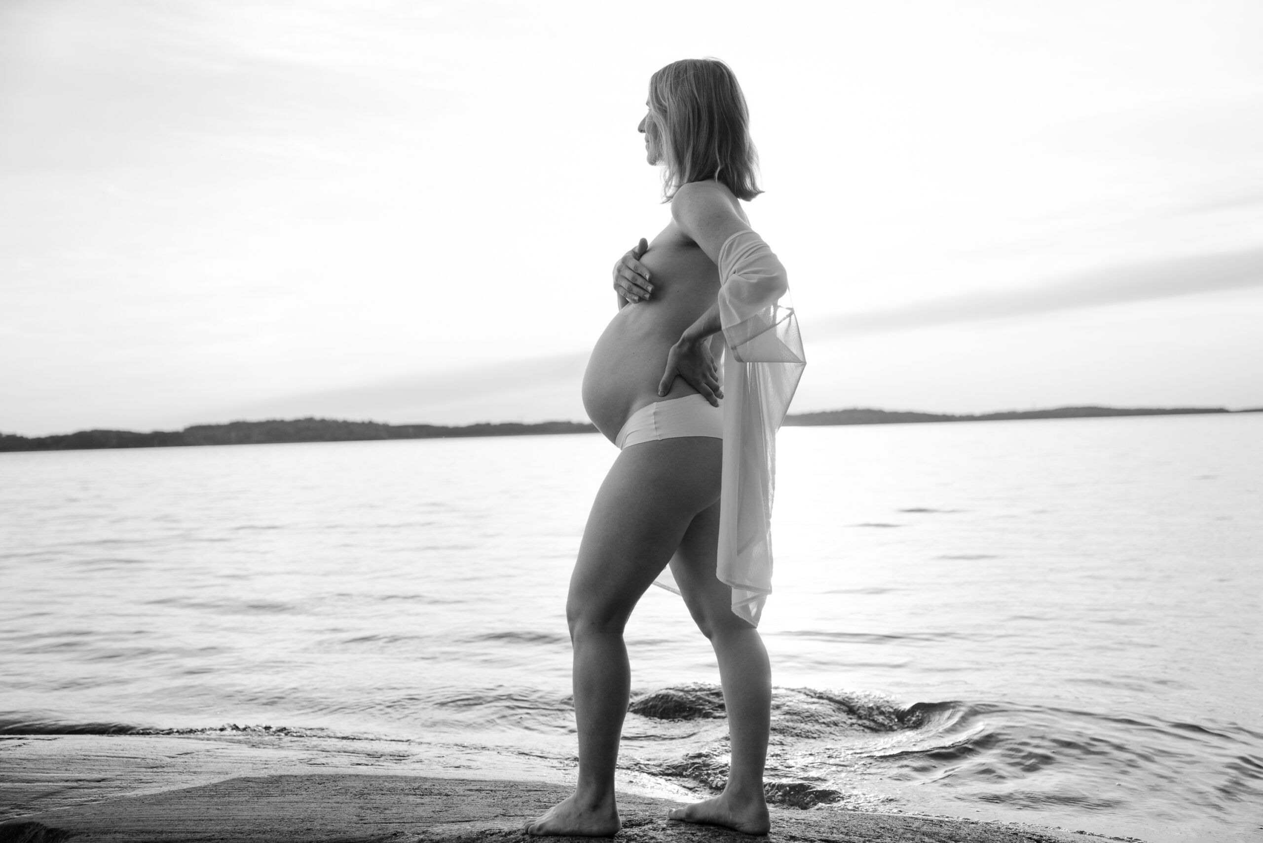 Svartvit bild på gravid kvinna vid havet.