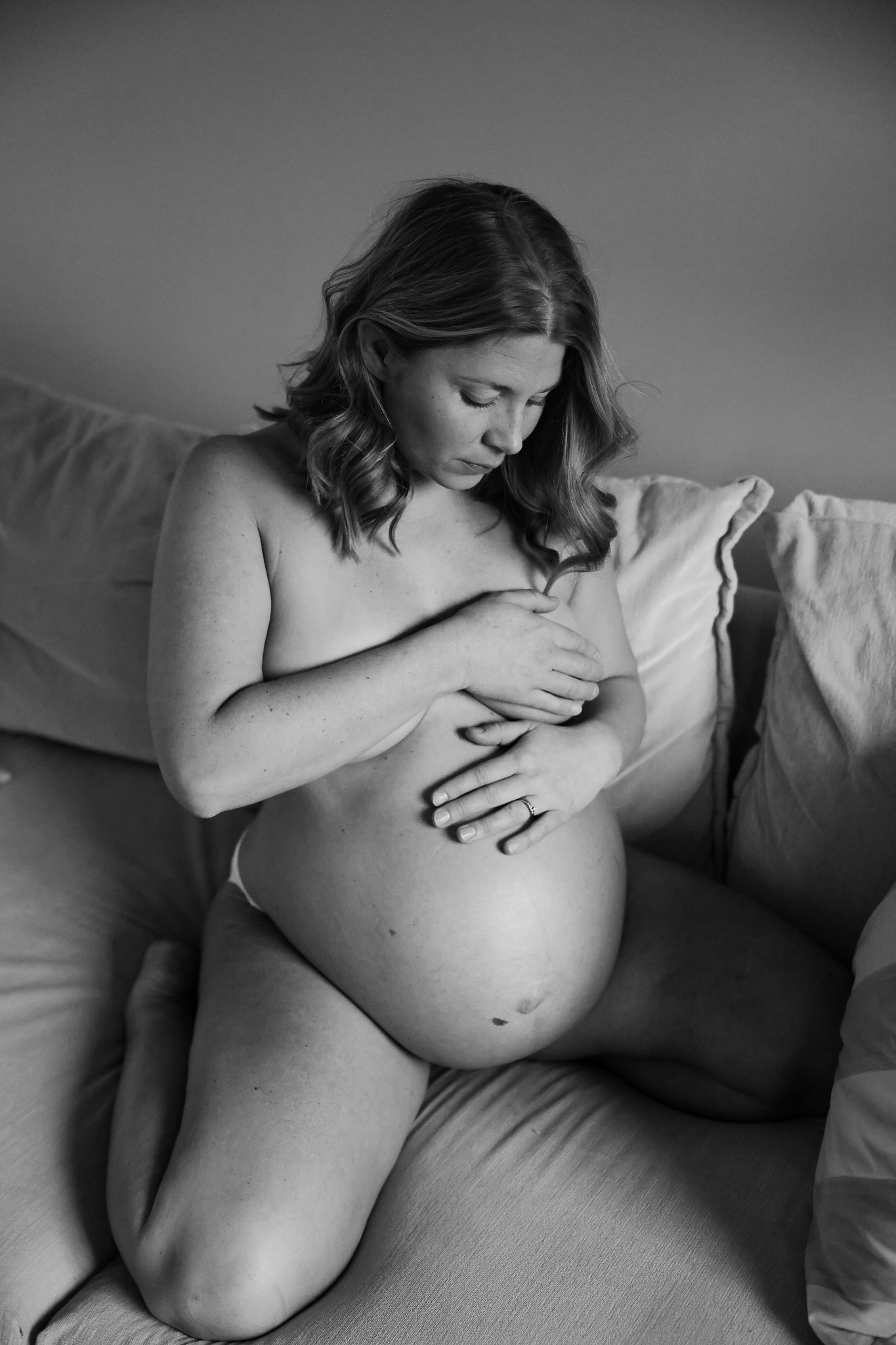 En gravid kvinna sitter i soffan i sitt eget hem.