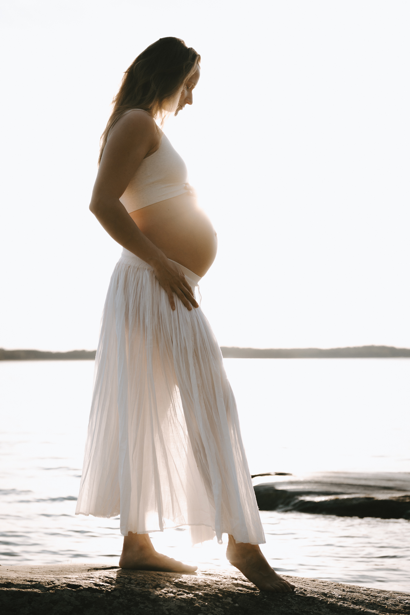 En gravid kvinna står på en klippa vid vattnet.