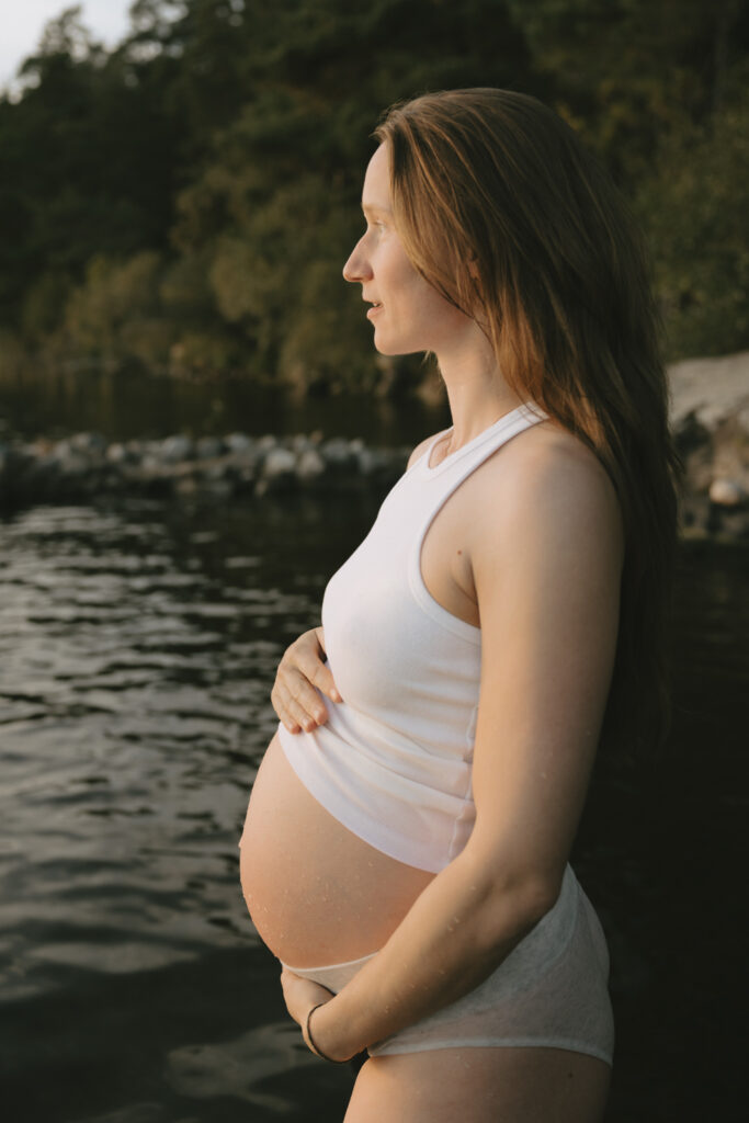 En gravid kvinna står i vattnet och håller händerna på magen.