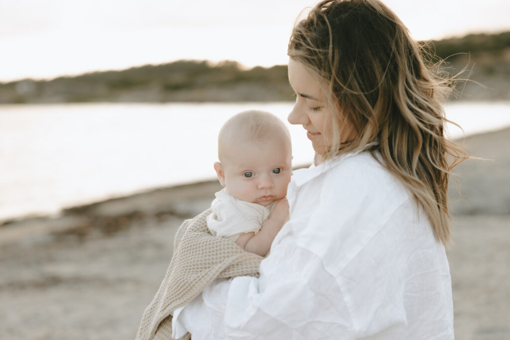En mamma håller sin bebis i famnen på stranden vid havet.