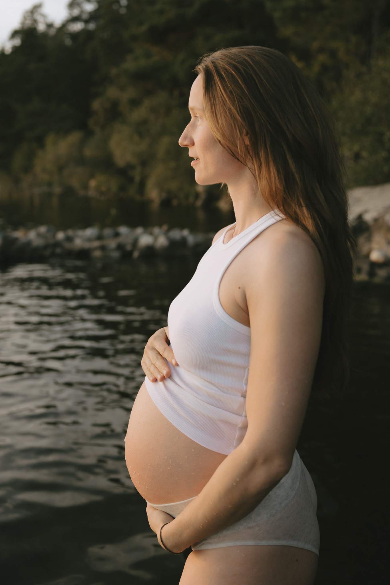 En gravid kvinna står i vattnet och håller händerna på magen.
