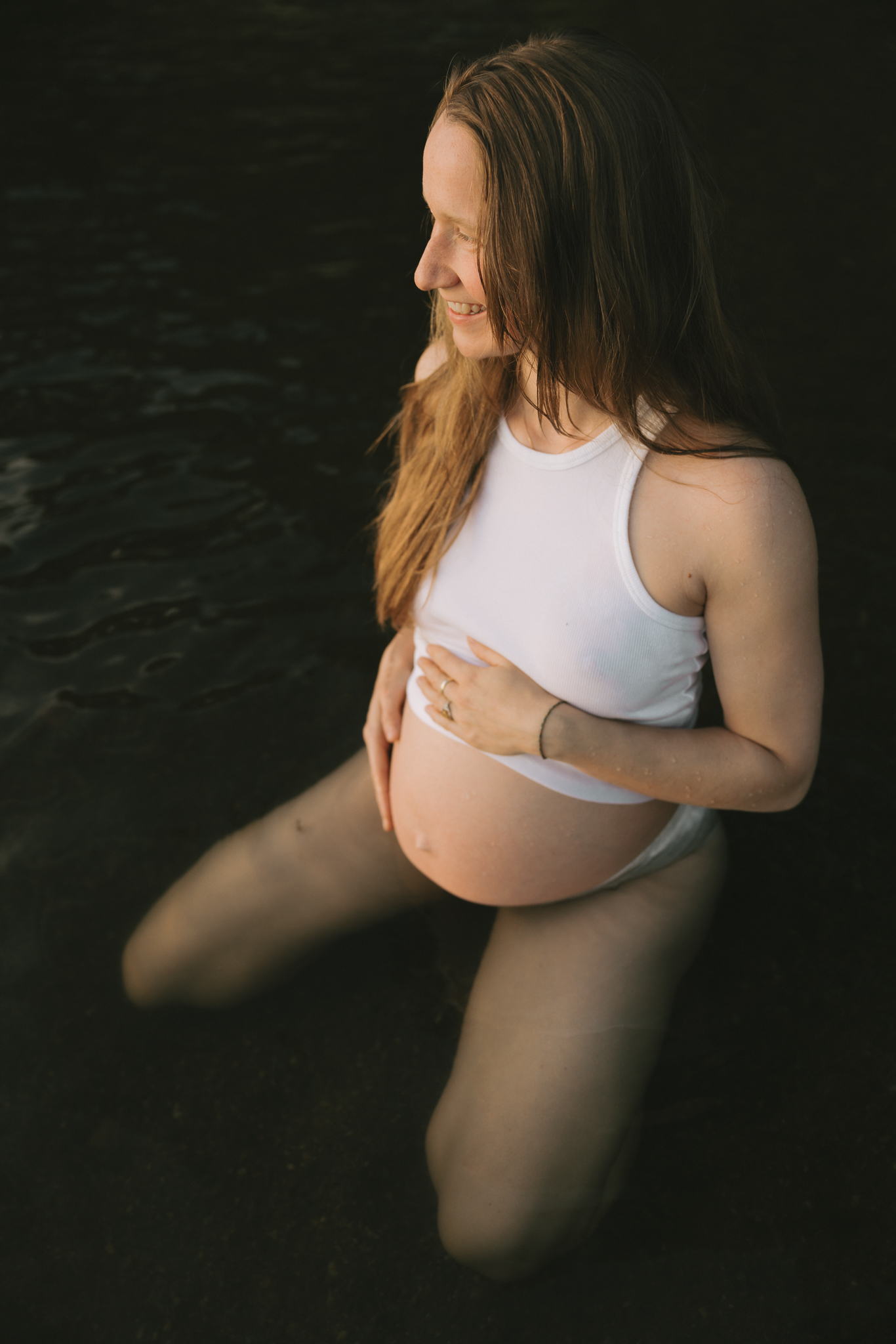 En gravid kvinna sitter i vattnet med handen på magen.