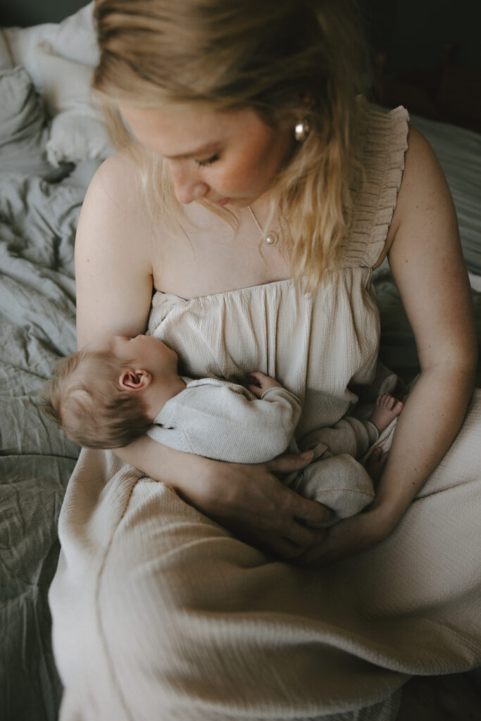 En mamma sitter i sängen med sin nyfödda bebis i famnen.