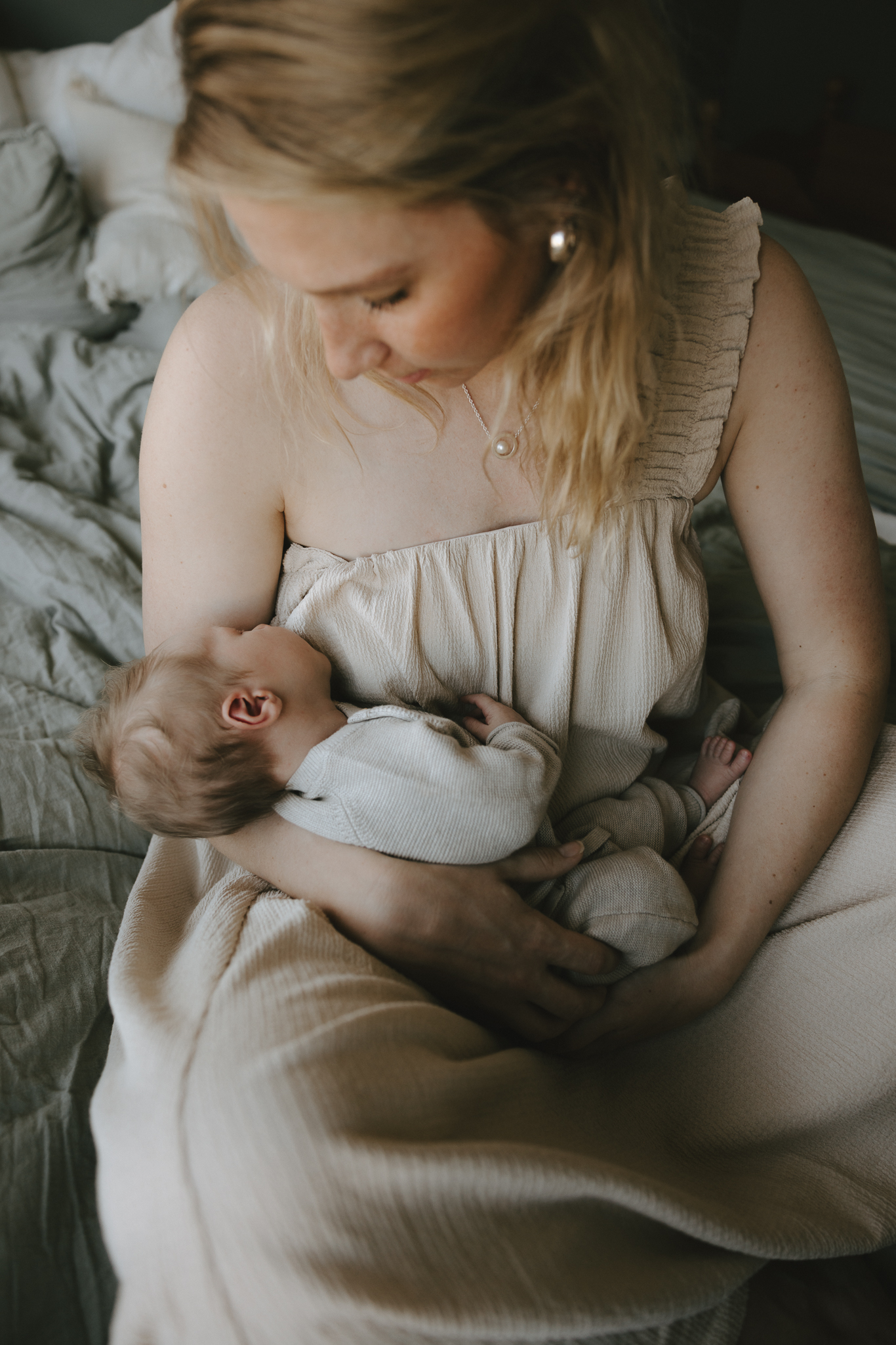 En mamma sitter i sängen med sin nyfödda bebis i famnen.