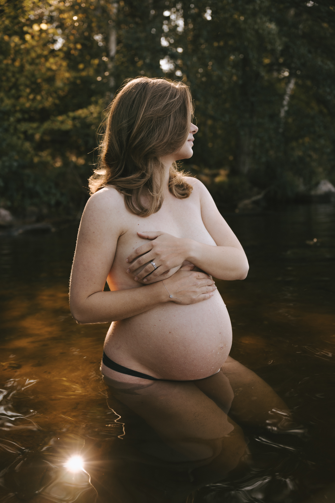 En gravid kvinna sitter på knä i vattnet.