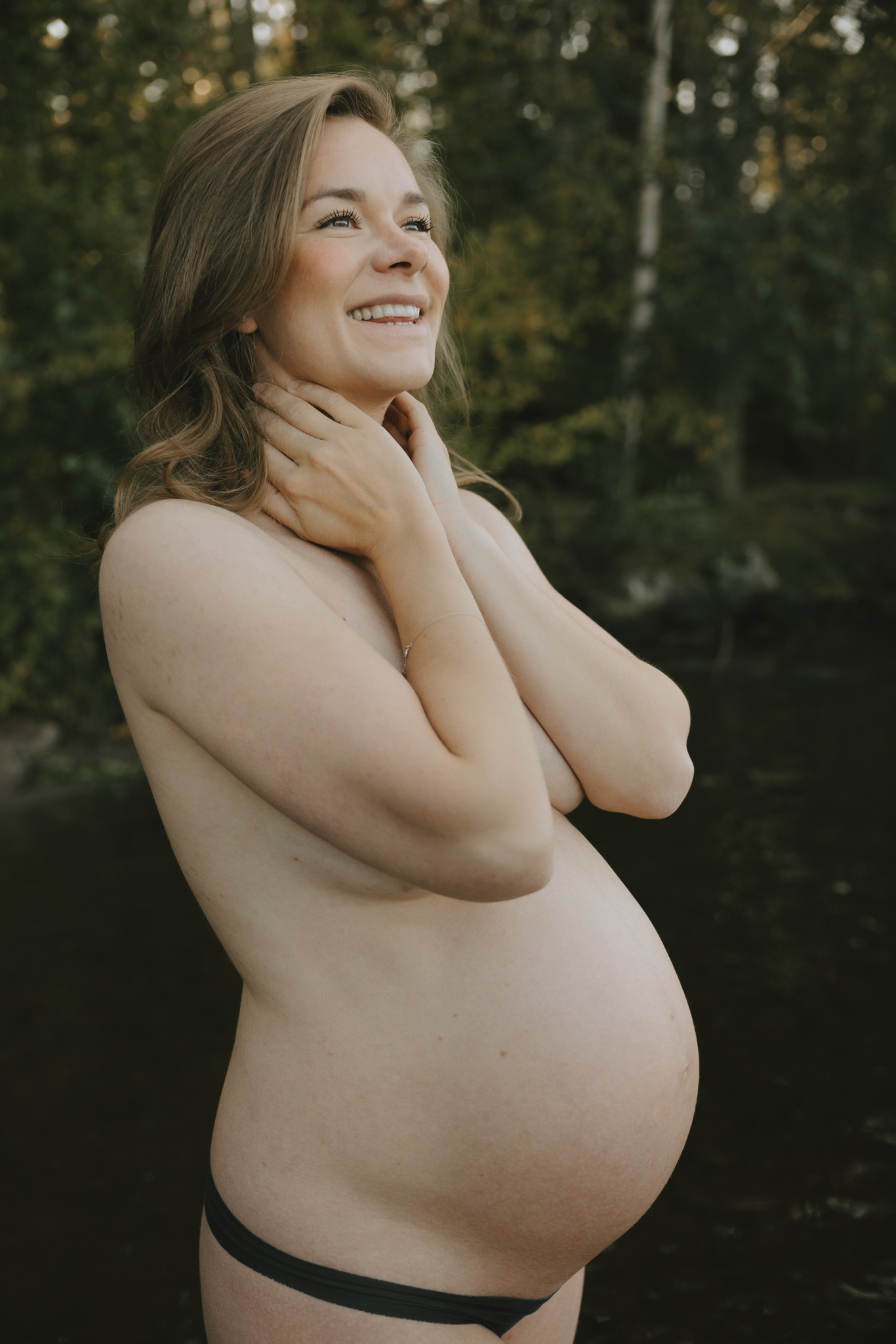 En gravid kvinna står i vattnet och håller händerna för brösten.