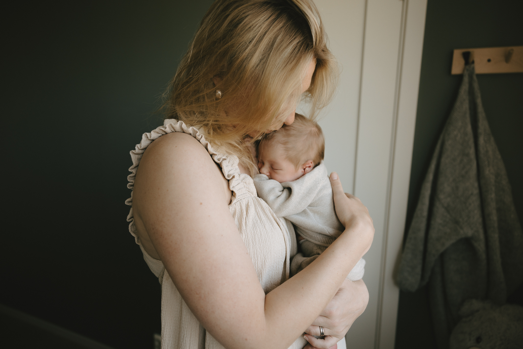 En nyfödd bebis ligger i mammas famn. Mamma pussar bebisen på huvudet.